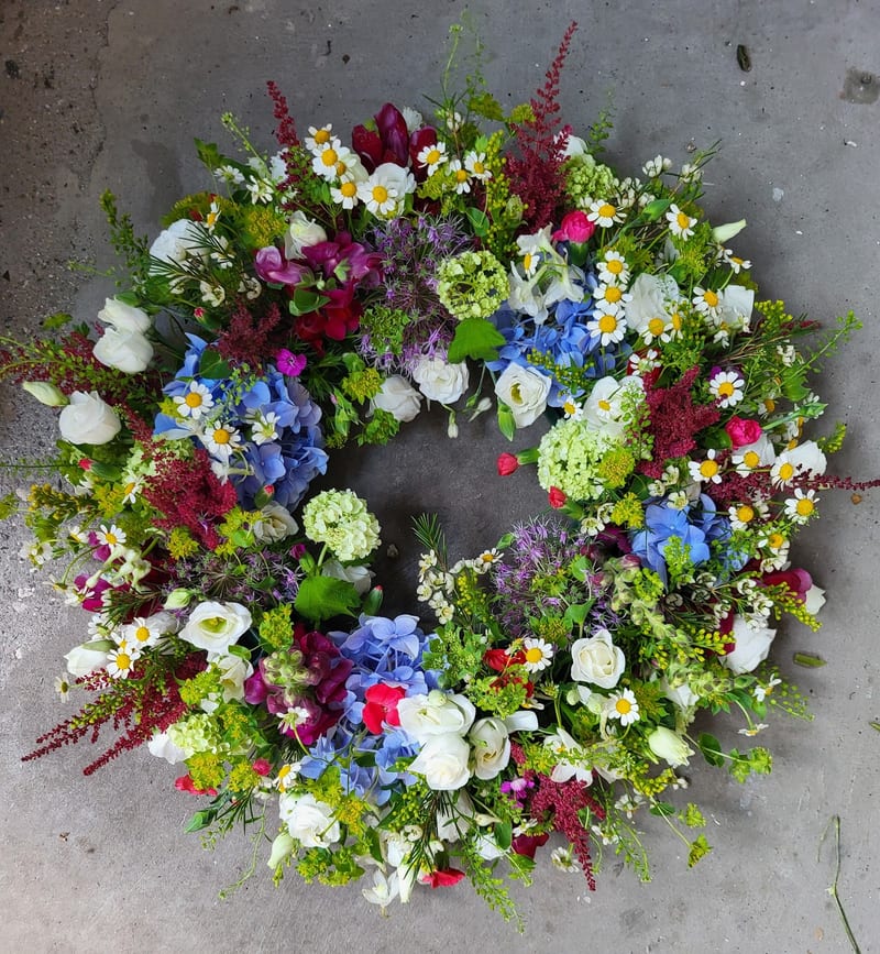 Krans af vildblomster, kamilier og blå blomster på stenfortov